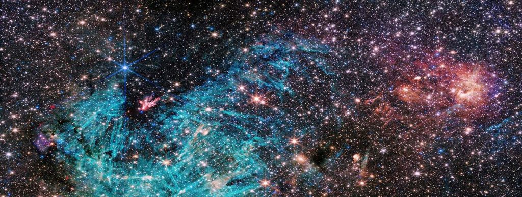 "Thiết bị NIRCam (camera cận hồng ngoại) trên kính viễn vọng không gian James Webb của NASA cho thấy một phần lõi dày đặc của Dải Ngân hà dưới một ánh sáng mới. Ước tính có khoảng 500,000 ngôi sao tỏa sáng trong hình ảnh này của vùng Nhân Mã C (Sgr C), cùng với một số đặc điểm chưa được xác định. Một vùng lớn hydro bị ion hóa, thể hiện bằng màu lục lam, chứa các cấu trúc hình kim hấp dẫn không có bất kỳ định hướng đồng nhất nào." | Credit: NASA, ESA, CSA, STScI, và S. Crowe (Đại học Virginia)